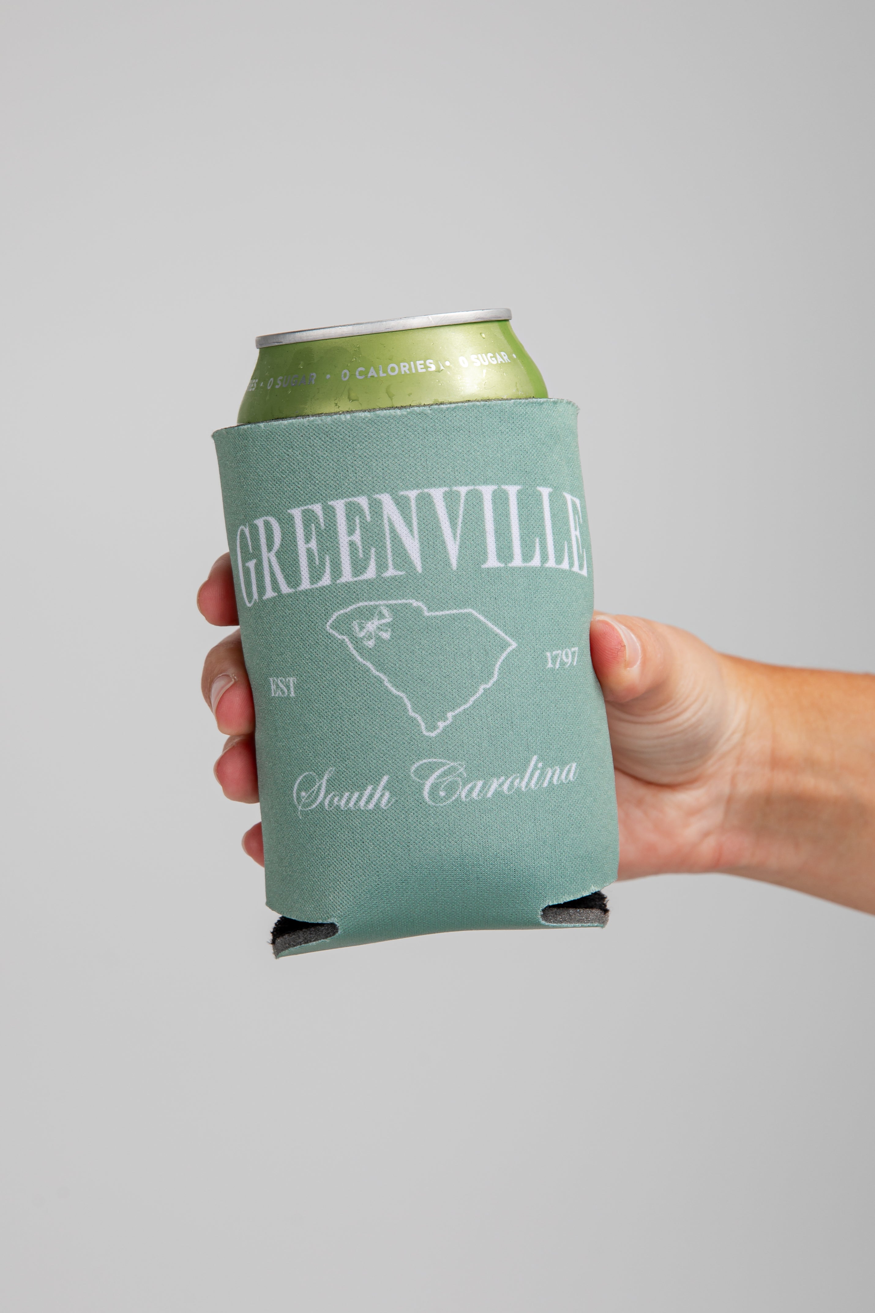 Hand holding a can with a Greenville, South Carolina design on a gray background
