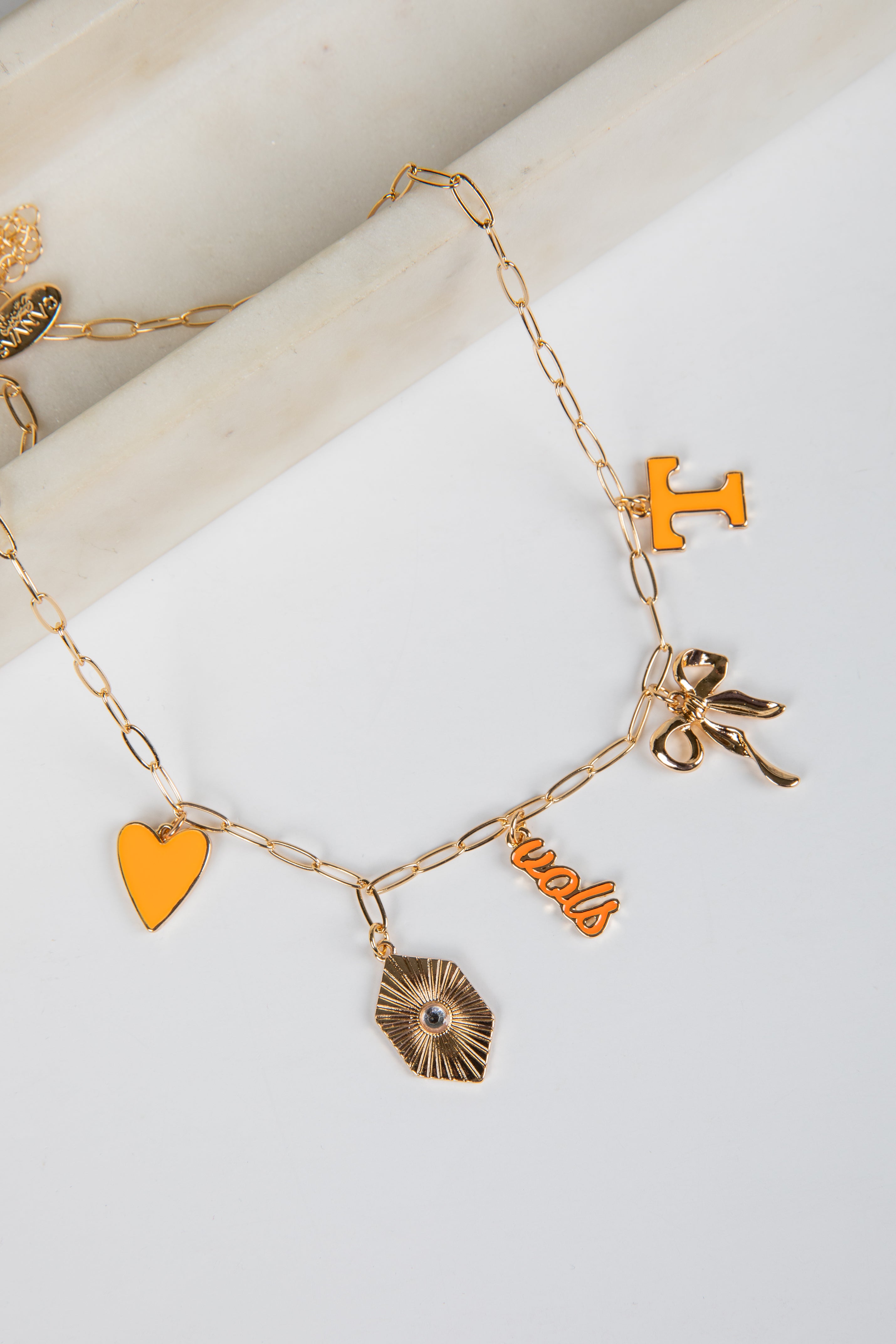 Gold bracelet with various charms including a heart, bow, and initials on a white background