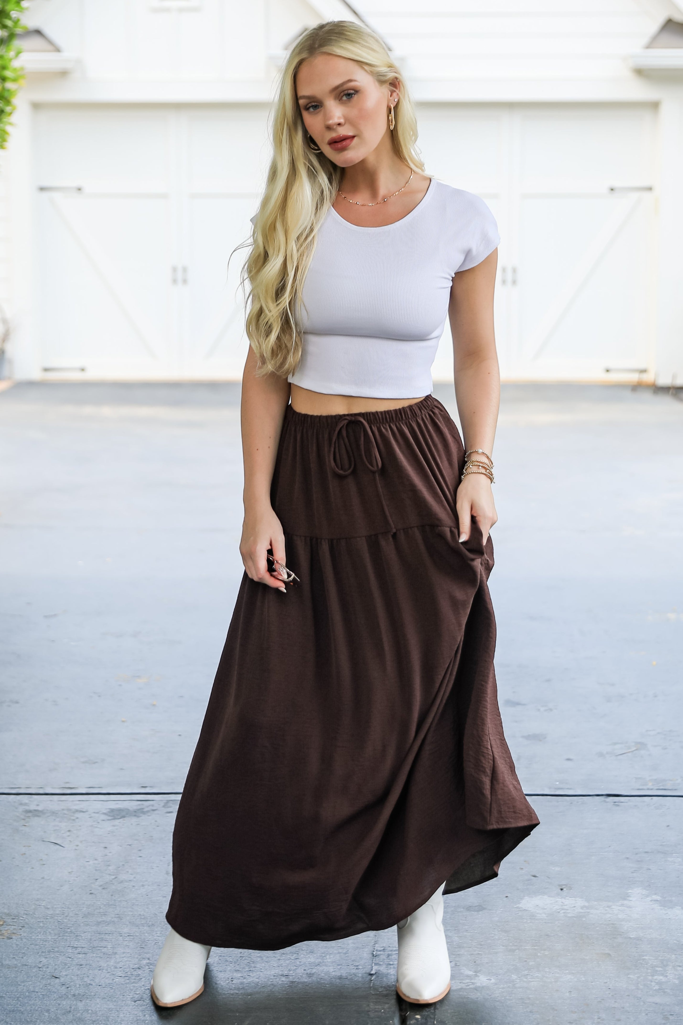 Woman wearing a white crop top and brown skirt standing in front of a white house.