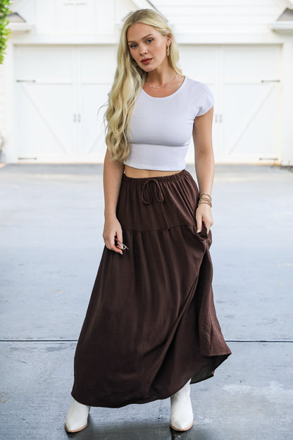Woman wearing a white crop top and brown skirt standing in front of a white house.
