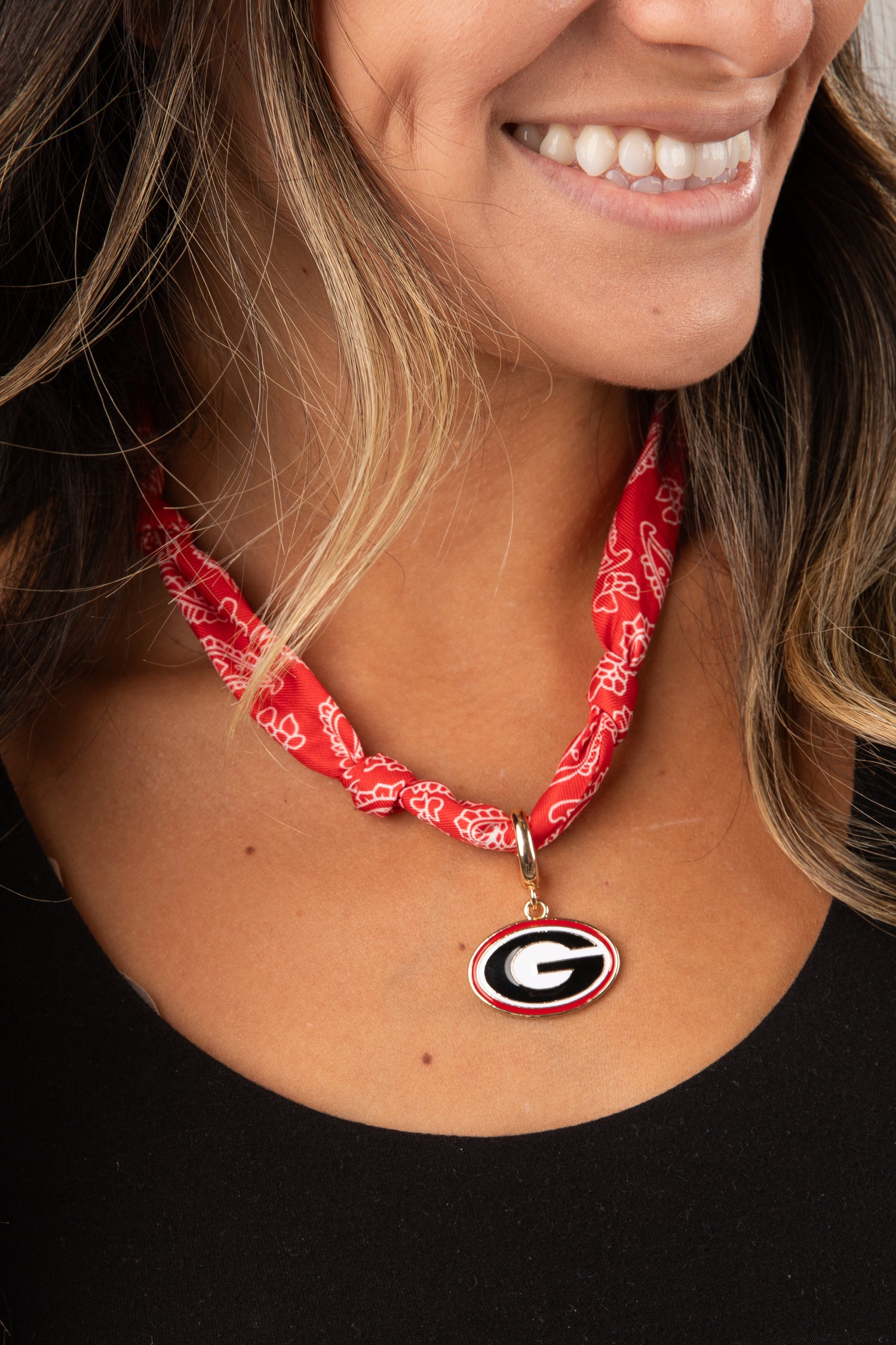 Person wearing a red bandana necklace with a logo pendant