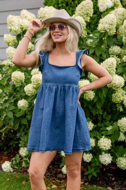 Woman in a blue dress and white boots standing in front of white flowers.