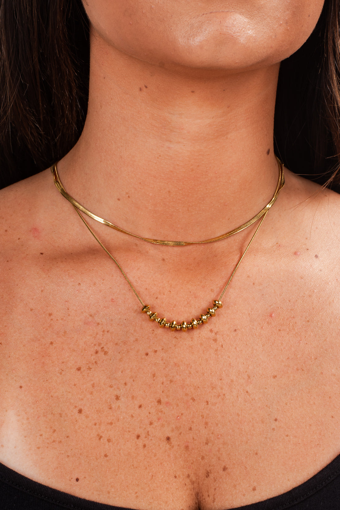 Close-up of a person wearing two gold necklaces on a dark background