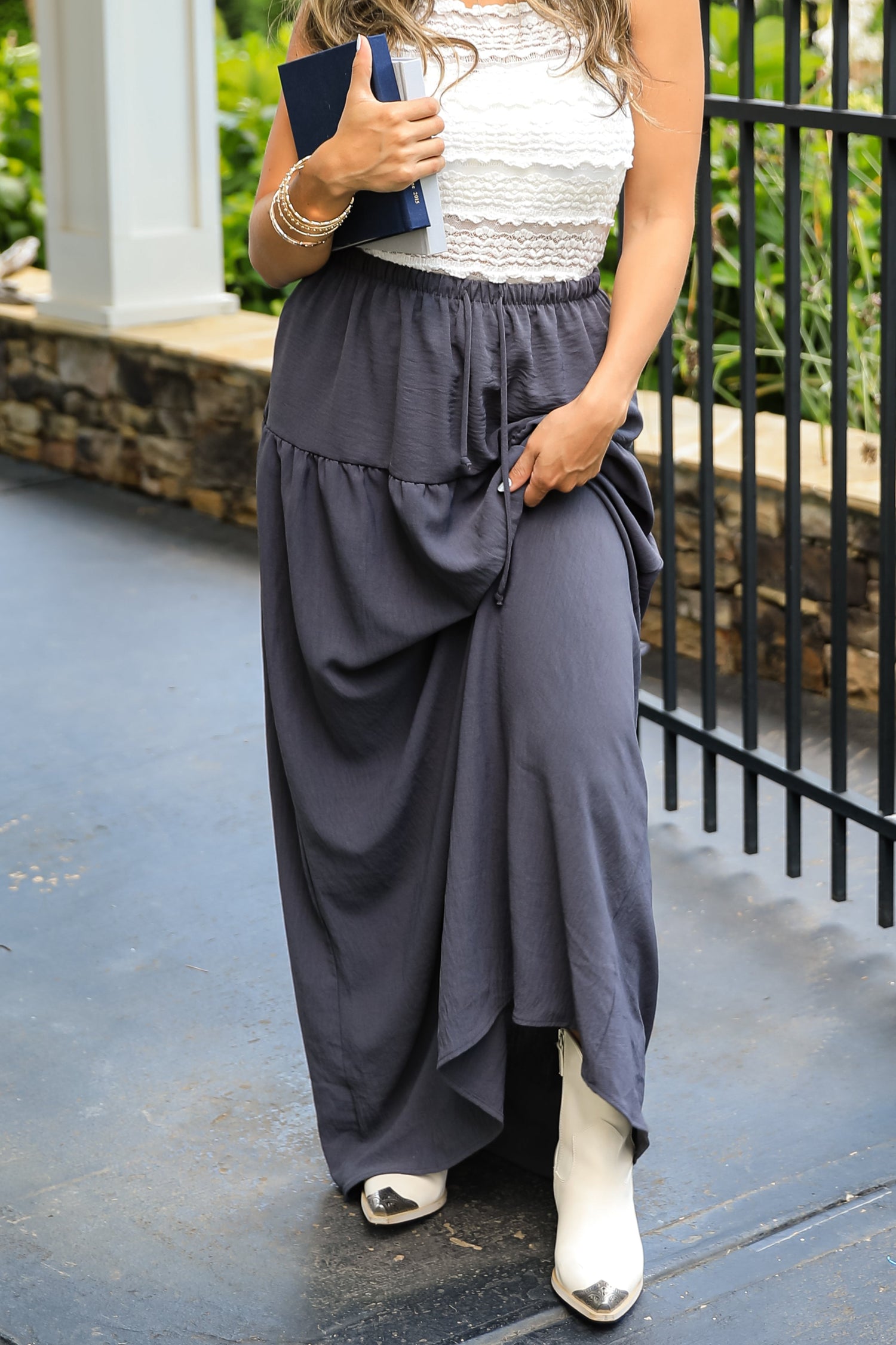 Woman wearing a white top and gray layered skirt with white shoes, holding a blue clutch.