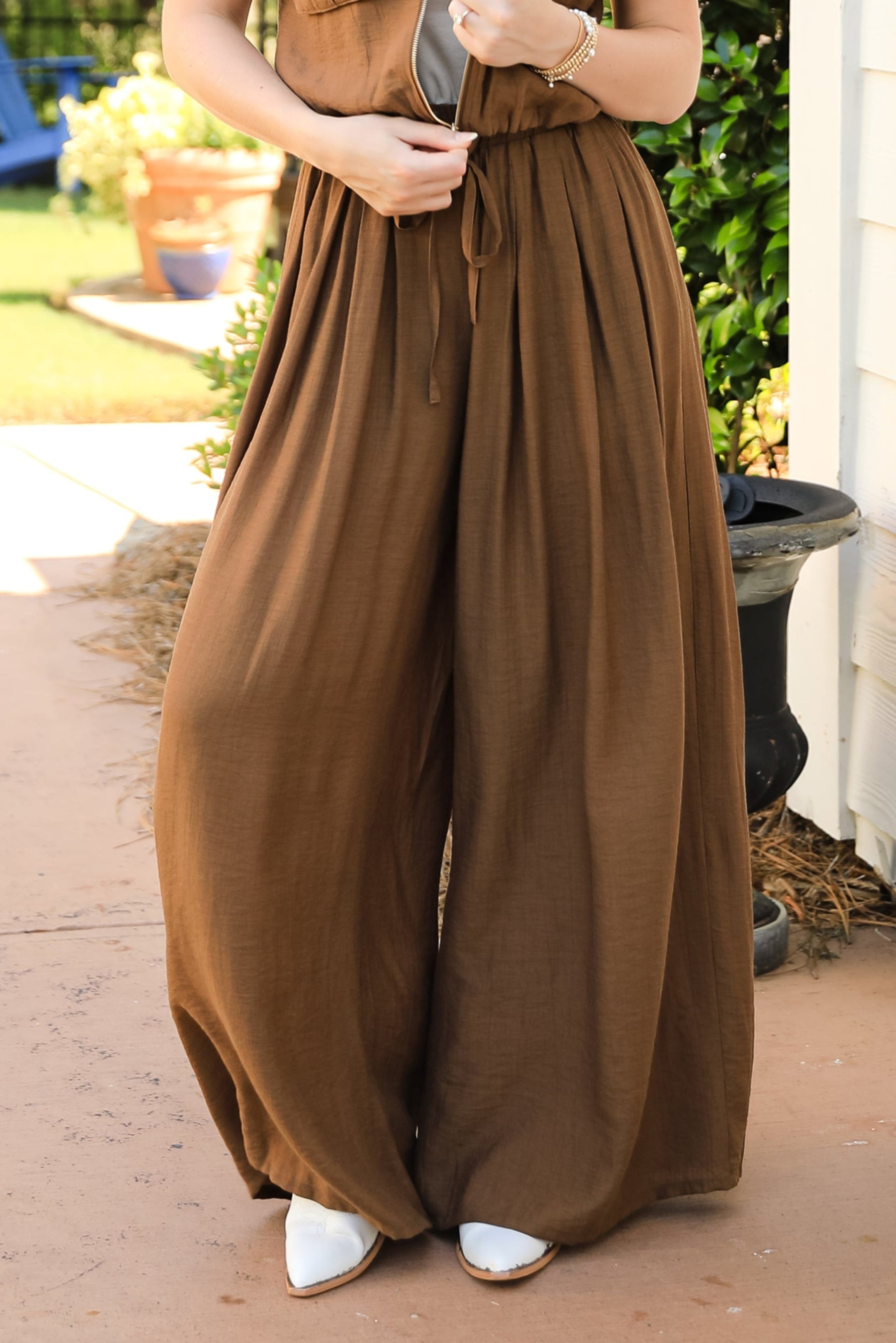 Woman wearing a brown jumpsuit standing on a porch.