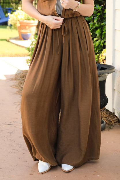 Woman wearing a brown jumpsuit standing on a porch.