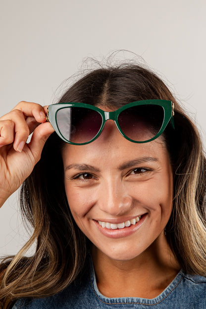 Woman holding green sunglasses up to her face against a plain background