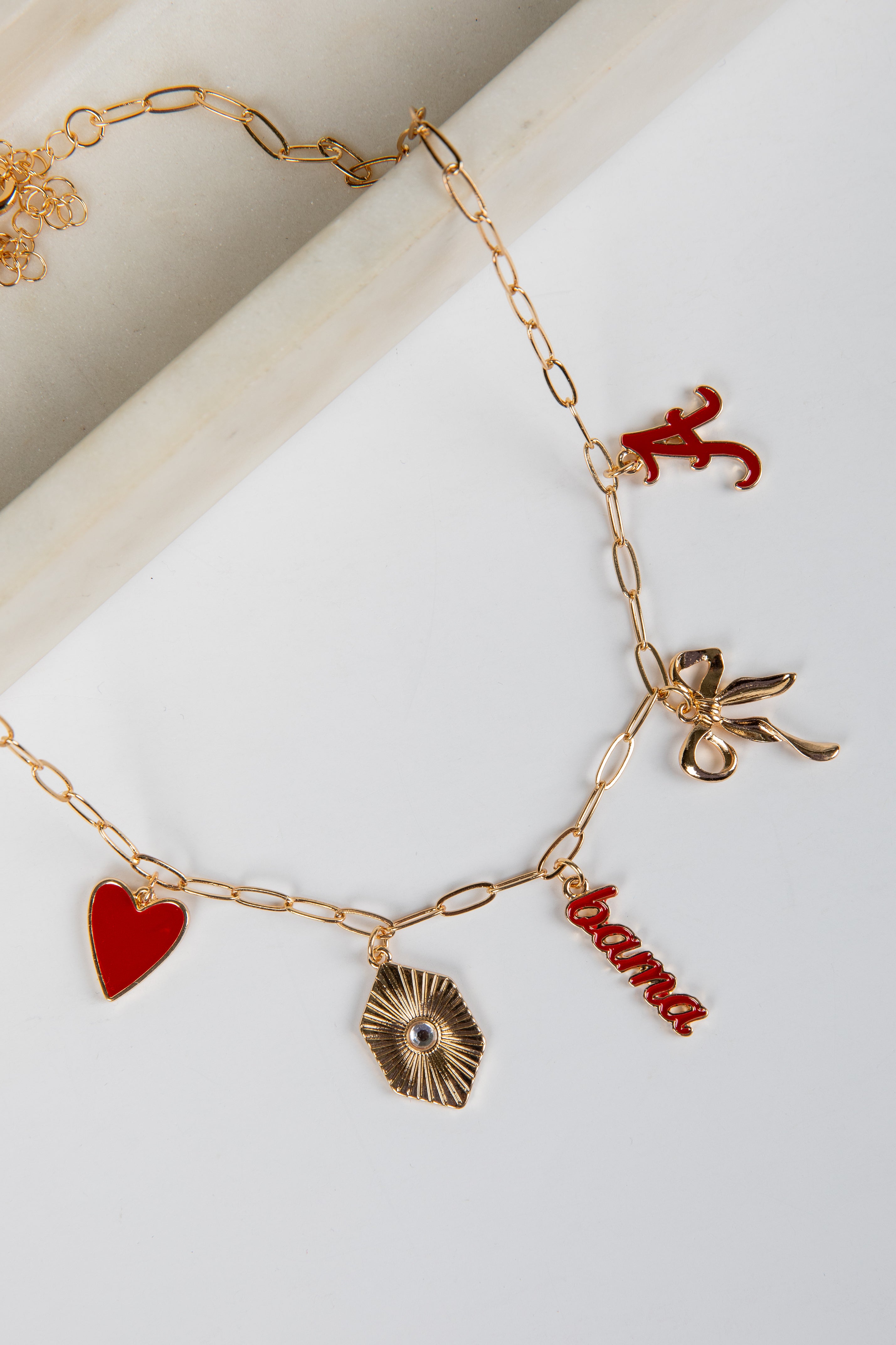 Gold bracelet with various charms including a red heart, leaf, and &