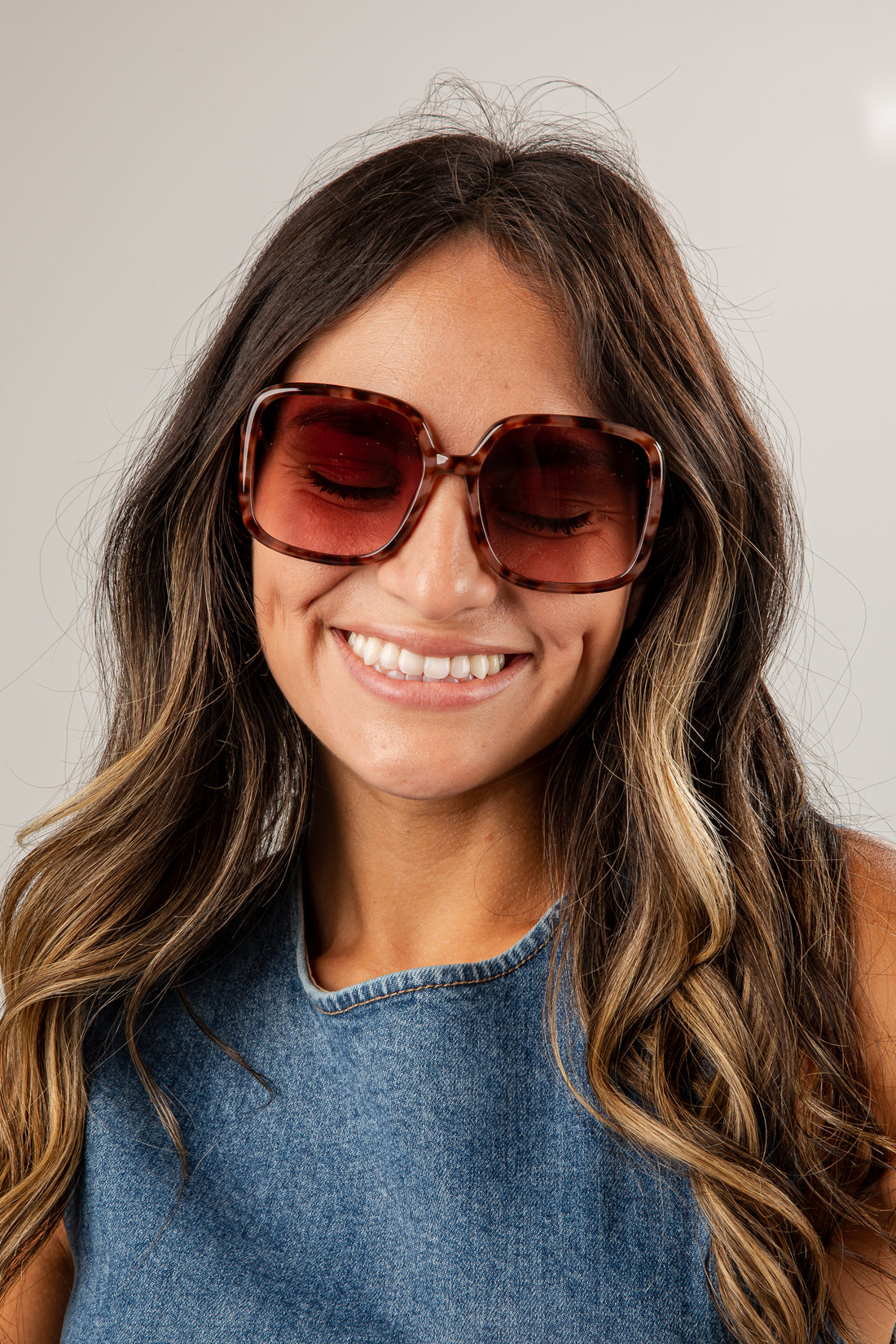 Woman wearing large sunglasses and a denim top against a plain background