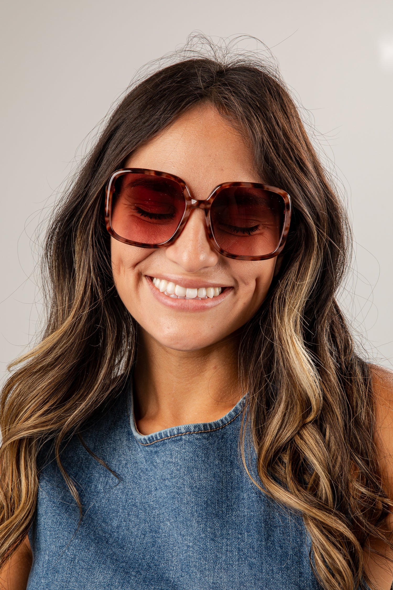 Woman wearing large sunglasses and a denim top against a plain background
