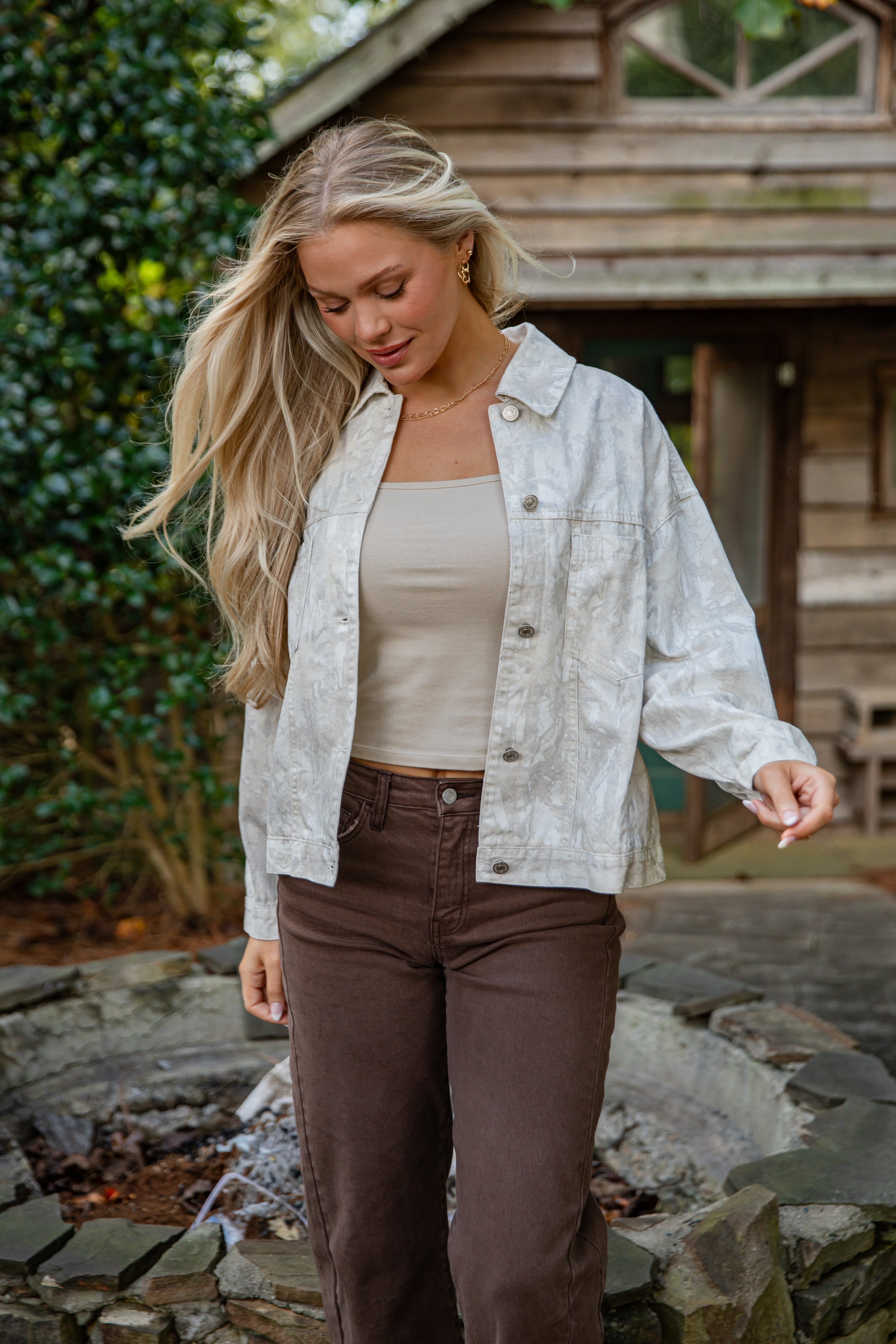 Woman wearing a light jacket over a beige top and brown pants outdoors.