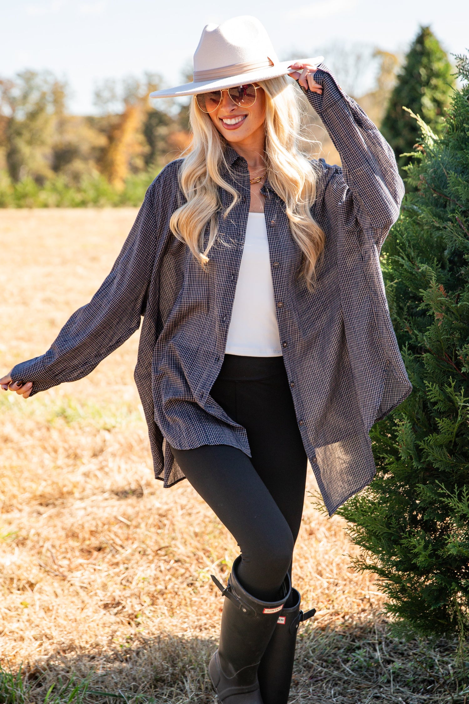 Woman in a gray coat and black boots standing in a field with trees in the background