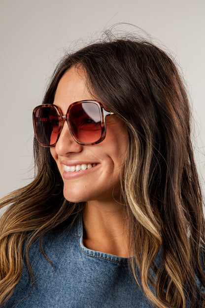 Woman wearing large sunglasses and a denim jacket against a neutral background