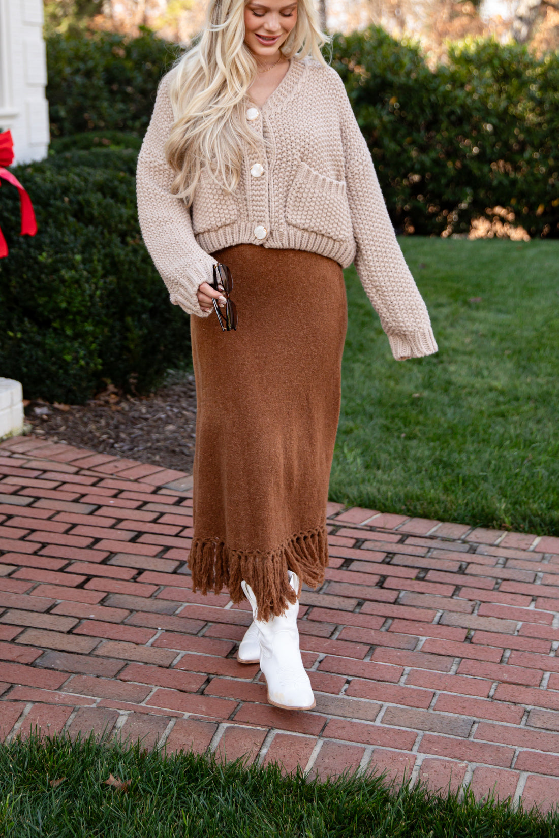 Woman wearing a beige cardigan and brown skirt outdoors on a brick path.