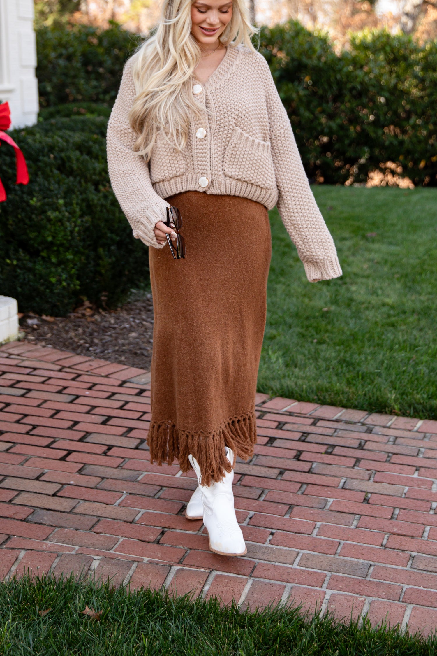 Woman wearing a beige cardigan and brown skirt outdoors on a brick path.