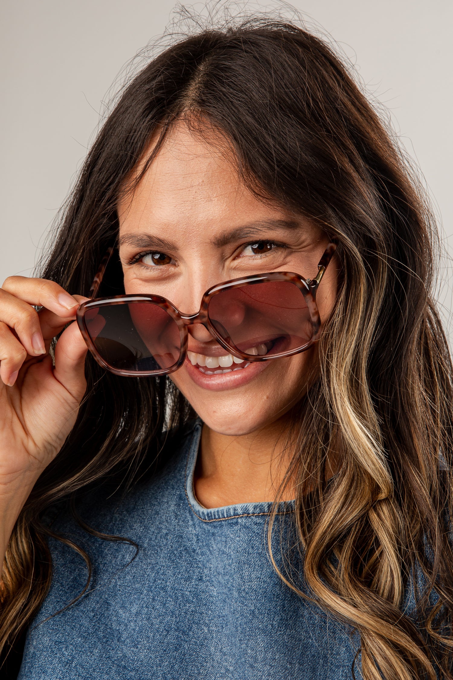 Woman holding sunglasses up to her face with a neutral background