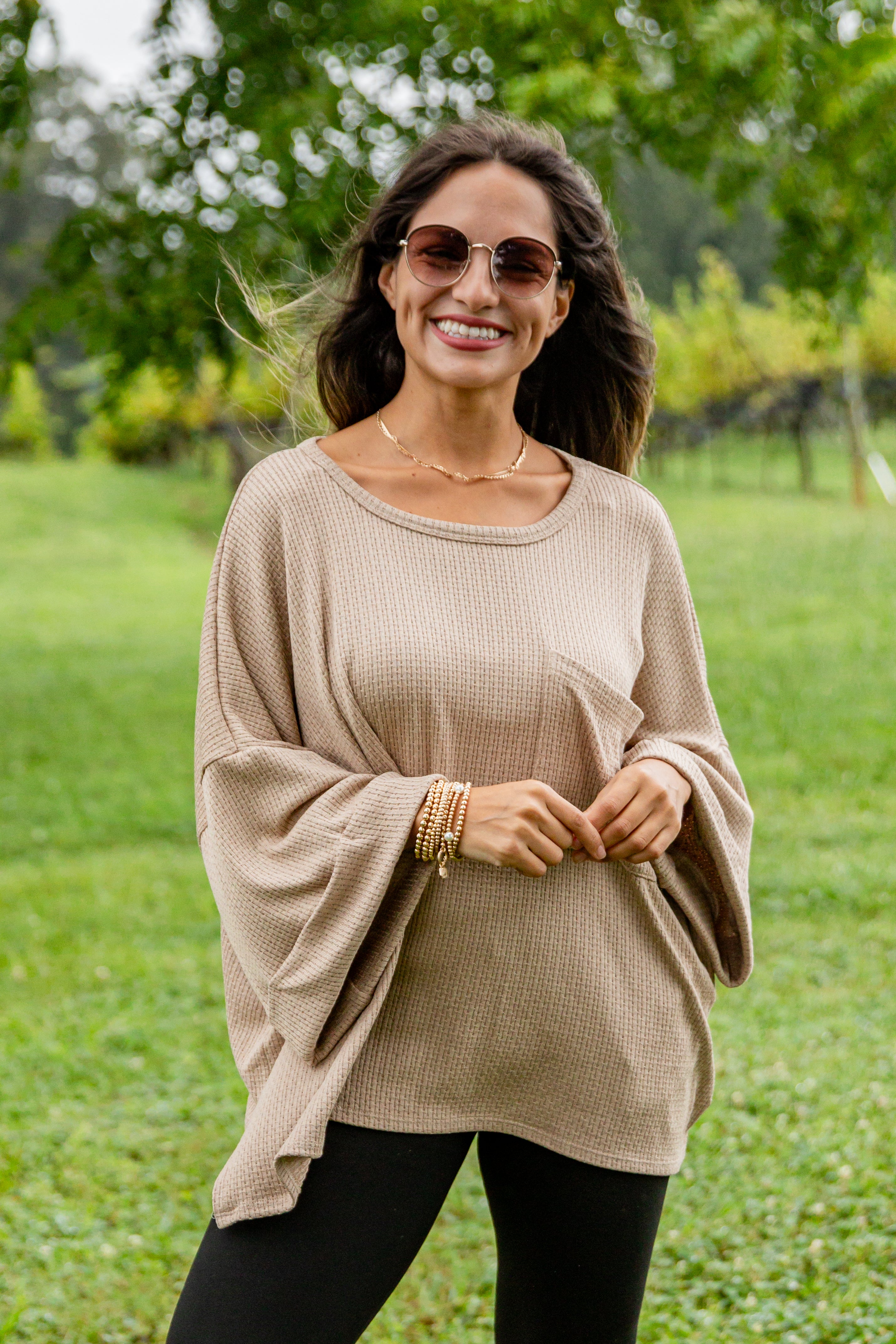 Woman wearing a beige sweater and sunglasses in a green outdoor setting