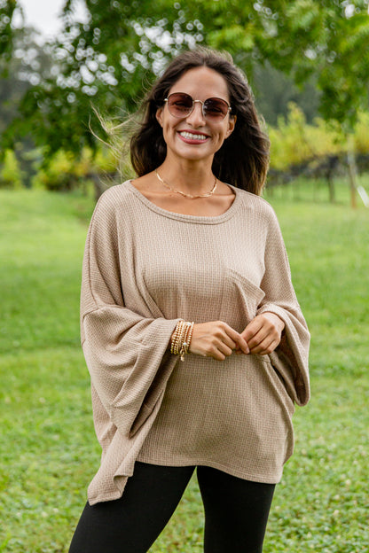 Woman wearing a beige sweater and sunglasses in a green outdoor setting