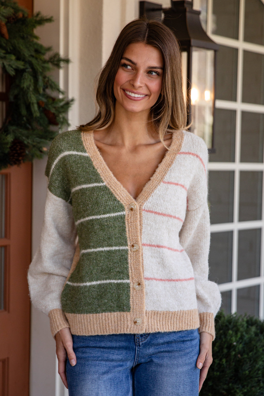 Woman wearing a patterned cardigan standing in front of a door with a wreath.