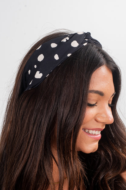 Woman wearing a black headband with white polka dots against a light background