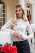Woman in a white lace top and black jeans standing on a porch with Christmas decorations.