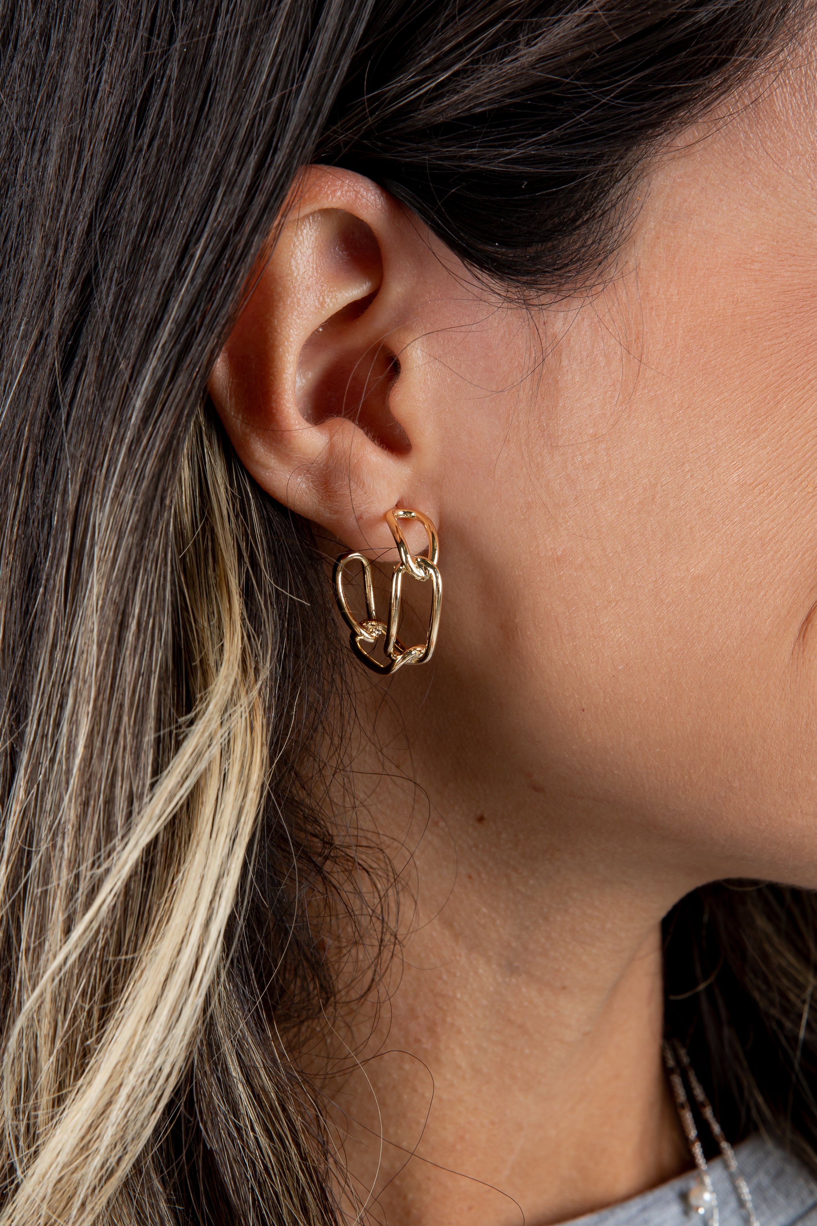 Close-up of a person wearing a gold hoop earring with hair and part of a denim shirt in the background.