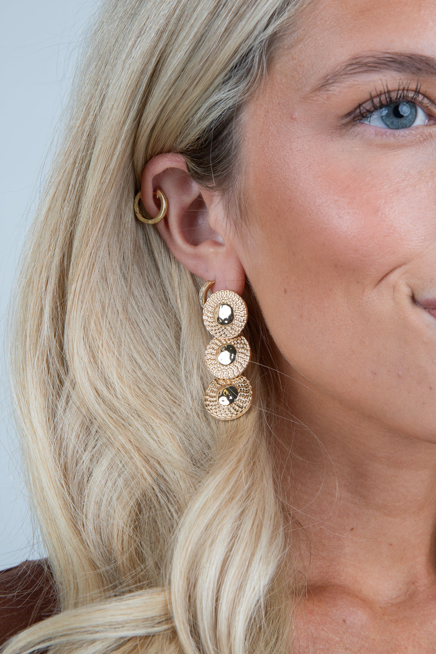 Close-up of a woman wearing gold earrings with a plain background