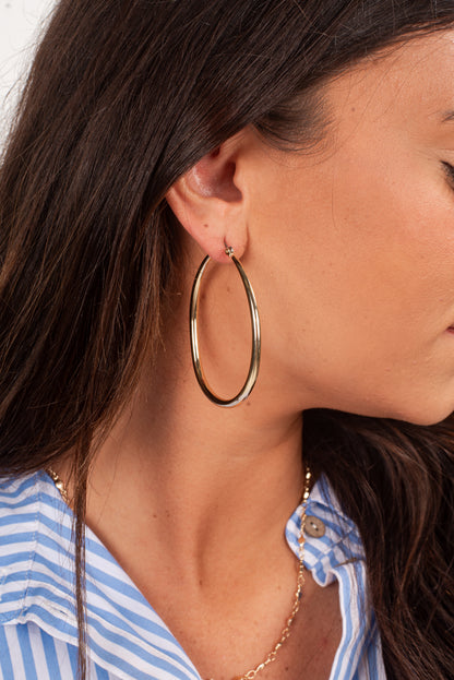 Close-up of a person wearing gold hoop earrings with a blurred background