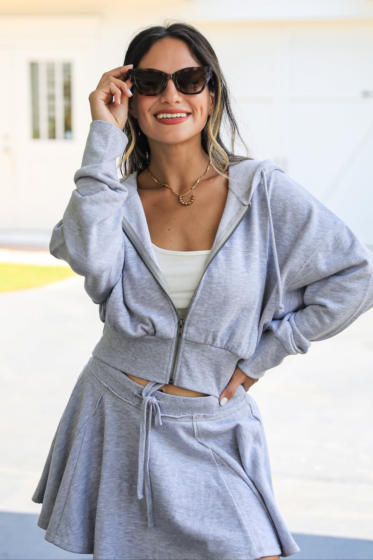 Woman wearing a gray tracksuit with sunglasses in an outdoor setting