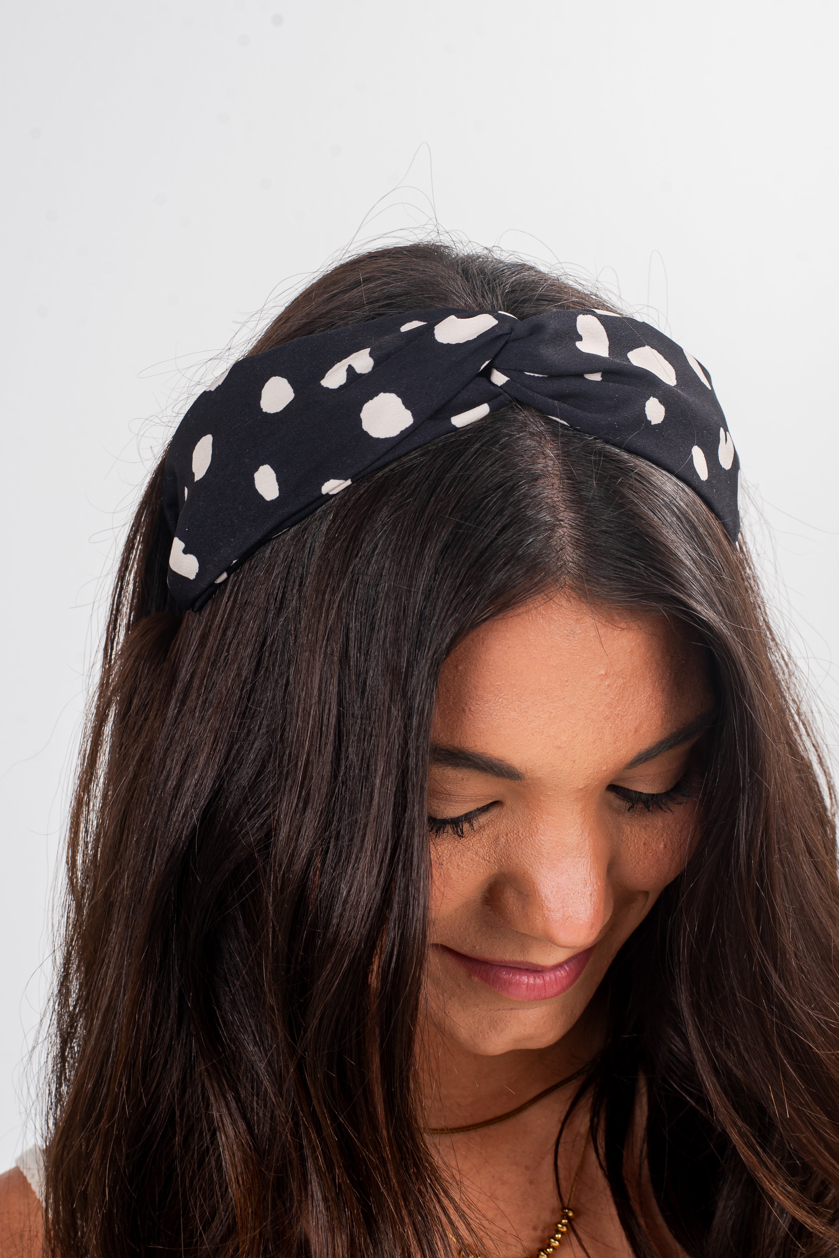 Woman wearing a black headband with white polka dots on a plain background