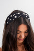 Woman wearing a black headband with white polka dots on a plain background