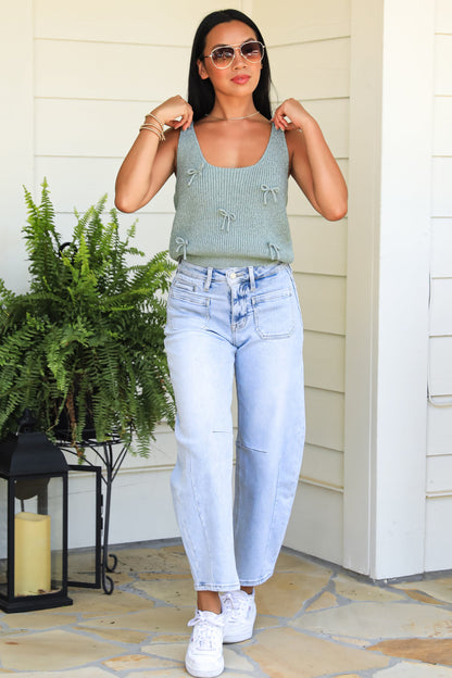 Woman wearing a green sleeveless top and light blue jeans standing on a stone patio.
