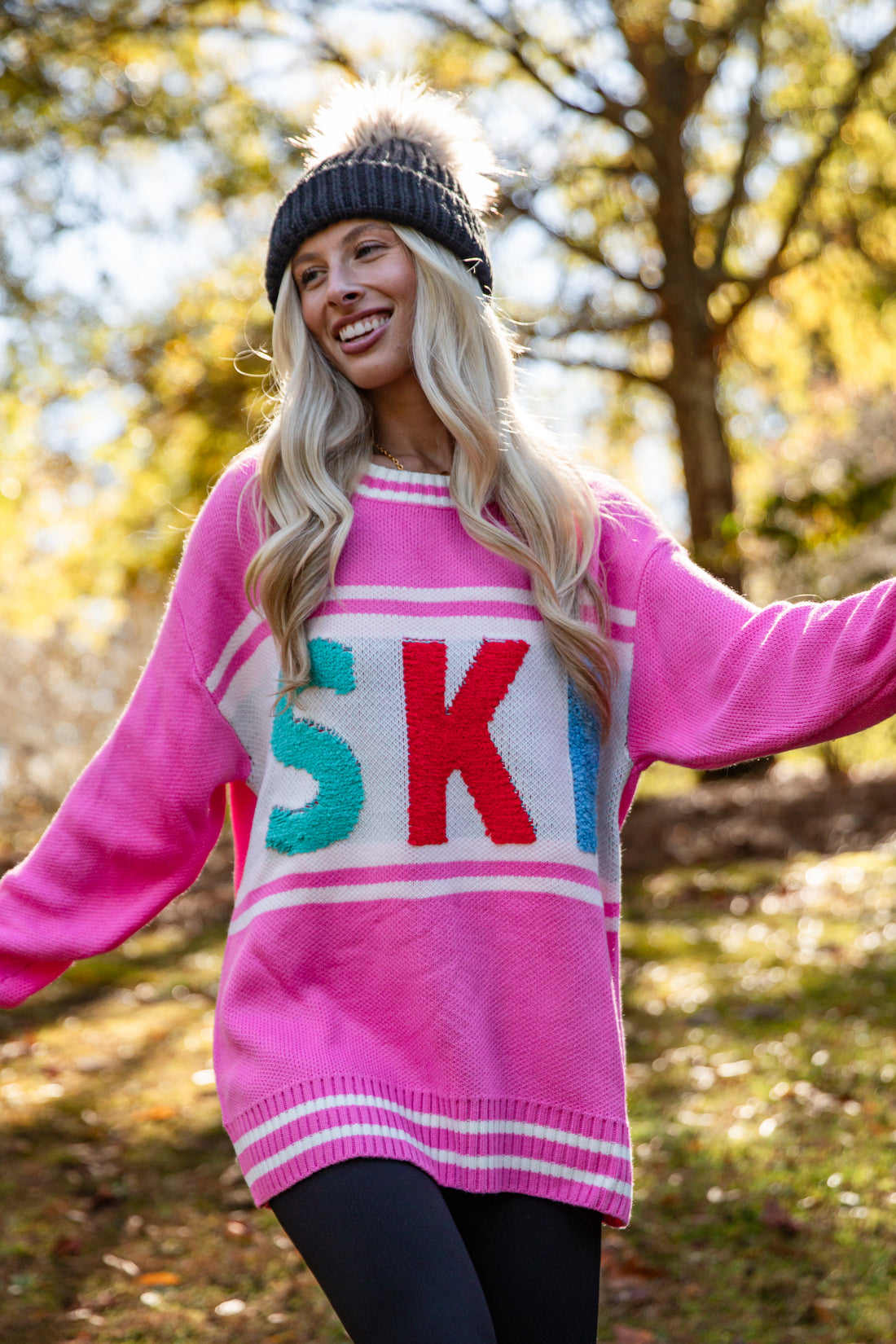 Person wearing a pink sweater with colorful letters in an outdoor setting