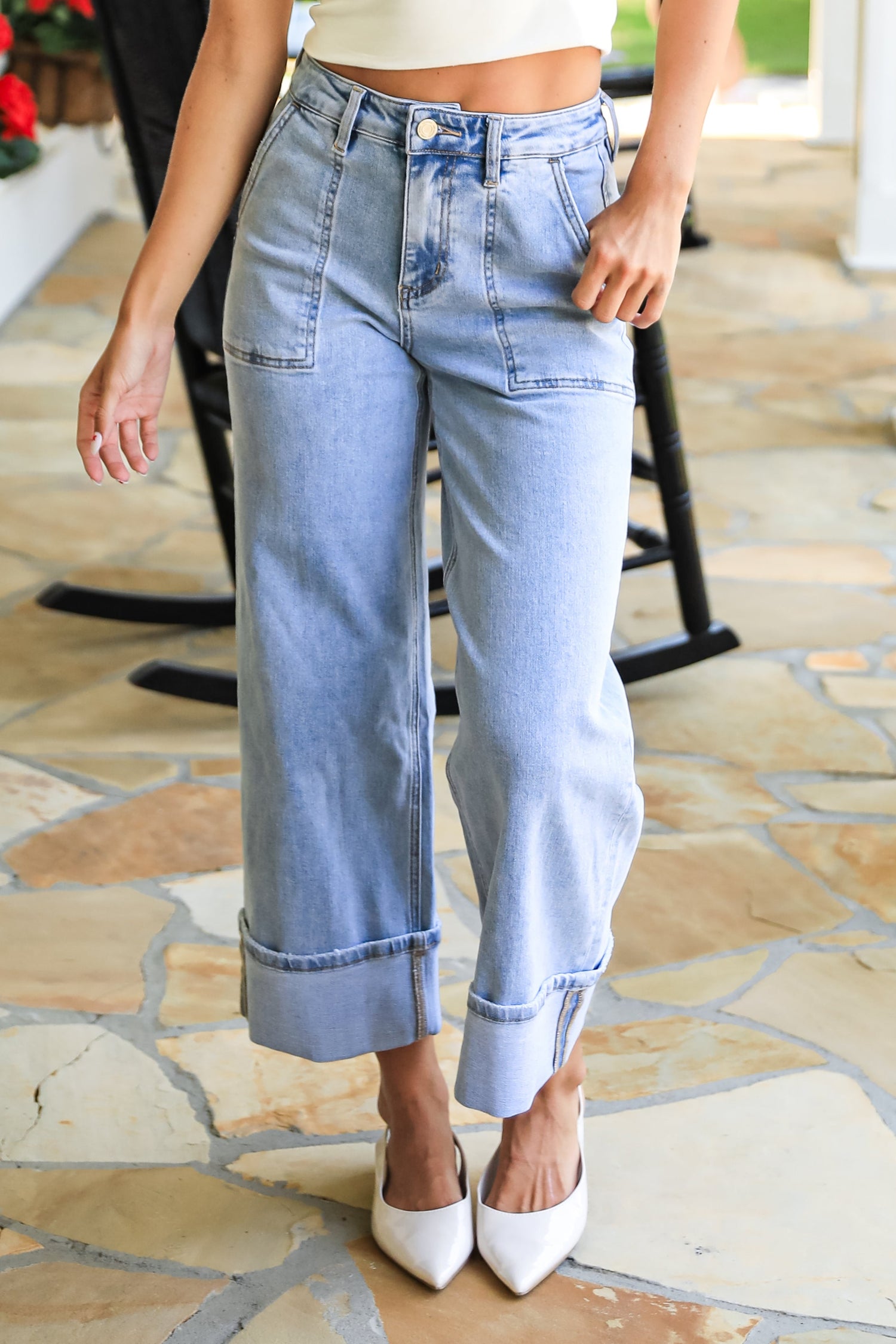 Person wearing light blue jeans and a white top on a stone patio.