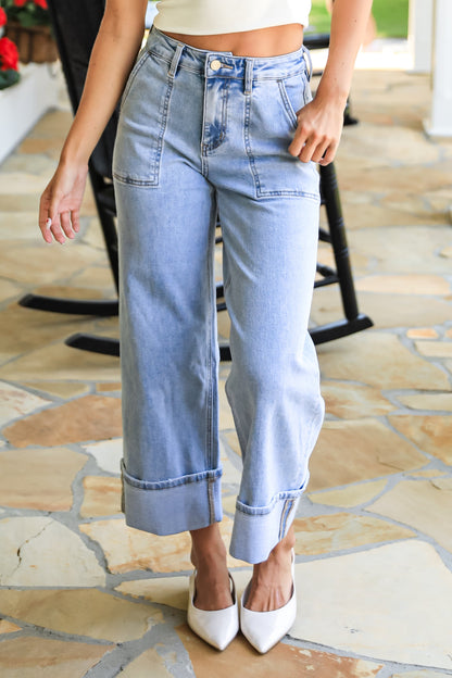 Person wearing light blue jeans and a white top on a stone patio.