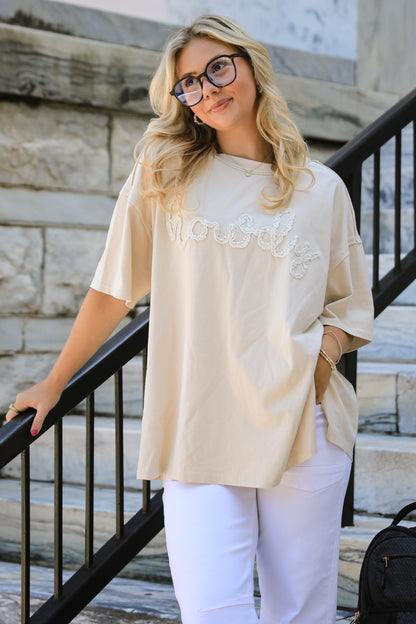 Woman in a beige top and white pants standing on stone steps with a black backpack.