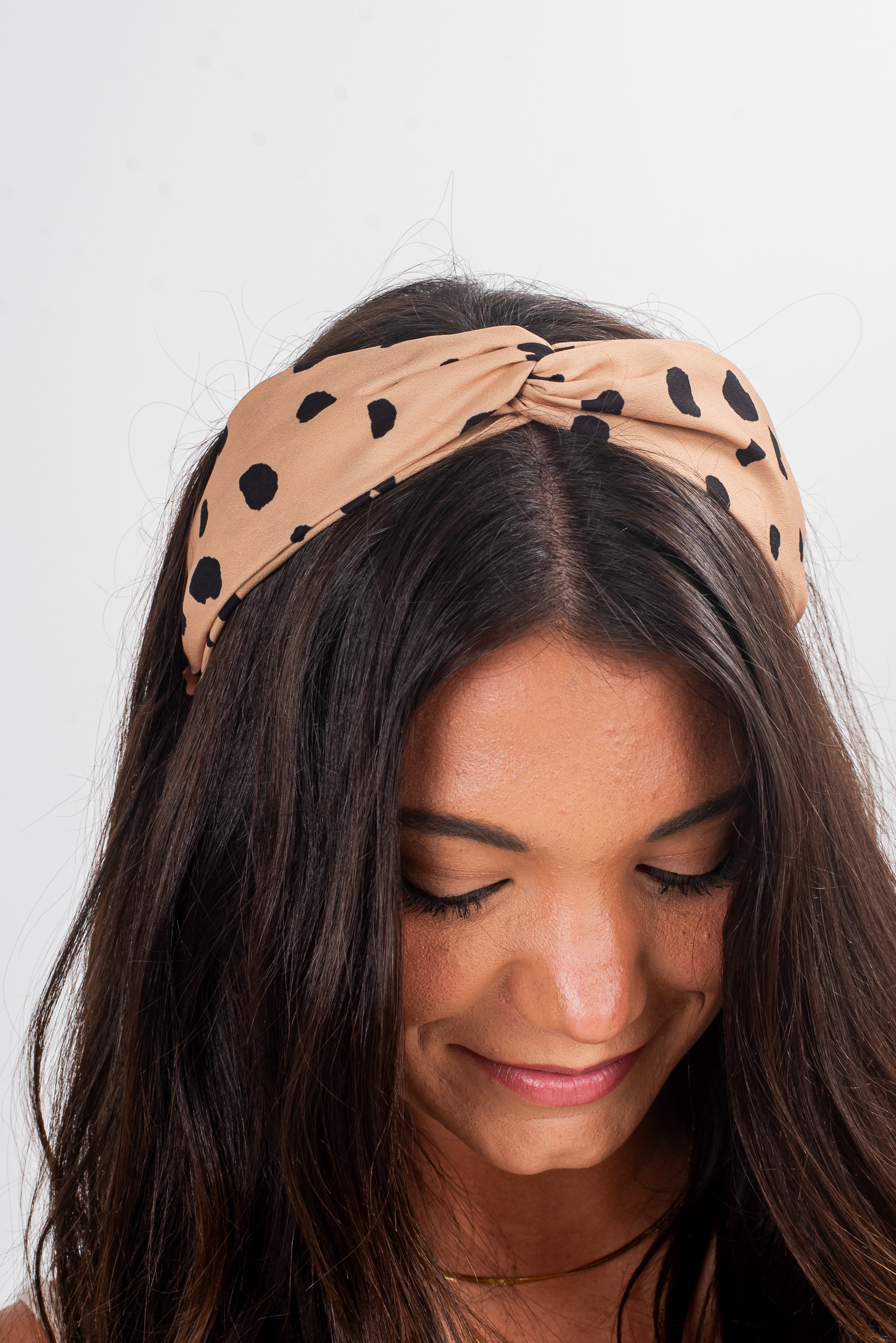 Woman wearing a beige headband with black polka dots on a white background