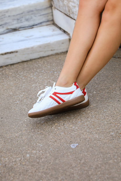 White sneakers with red stripes worn by a person on a concrete surface.