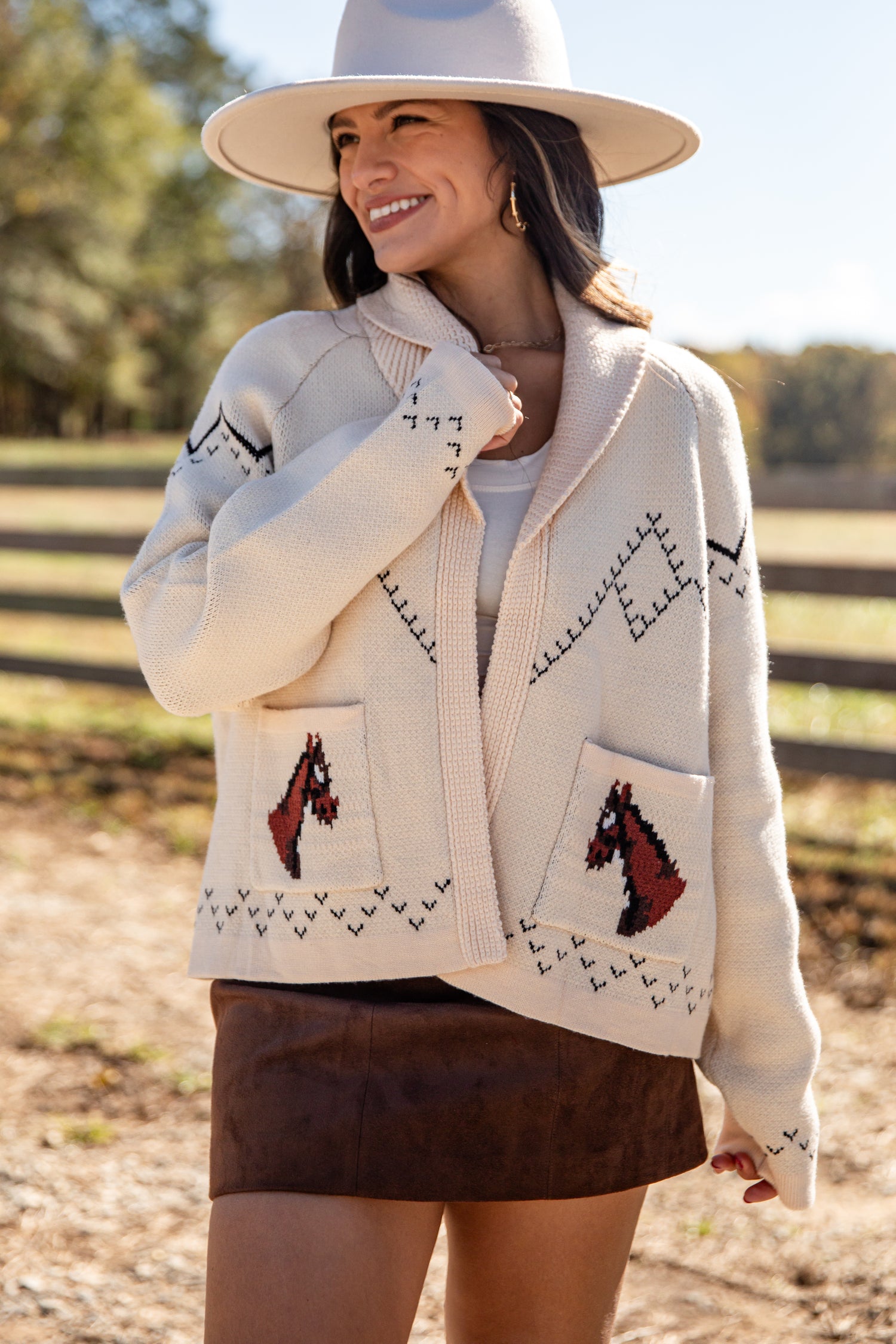 Woman wearing a cream-colored cardigan with horse designs outdoors.