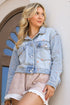 Woman wearing a denim jacket and skirt standing against a white wall.