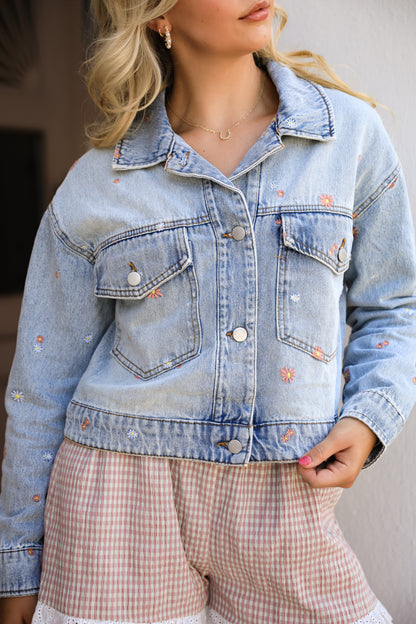Person wearing a light blue denim jacket with floral embroidery.
