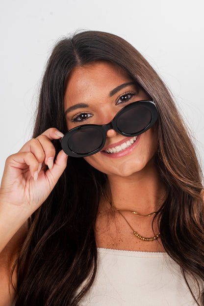 Woman holding black sunglasses up to her face against a white background