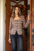 Woman wearing a plaid shirt and jeans standing in front of a door with autumn decorations.