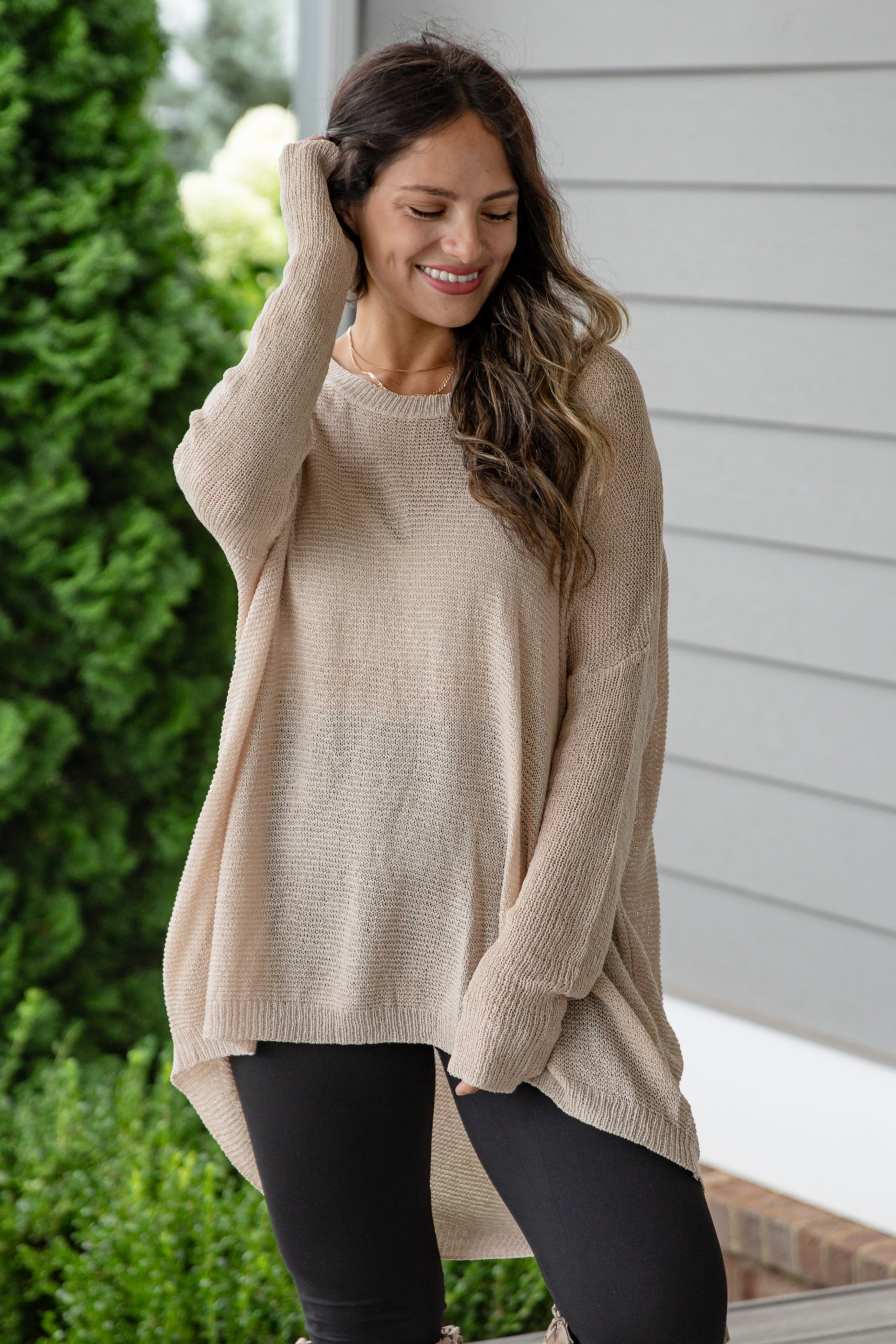 Woman wearing a beige sweater and knee-high boots on a wooden deck.