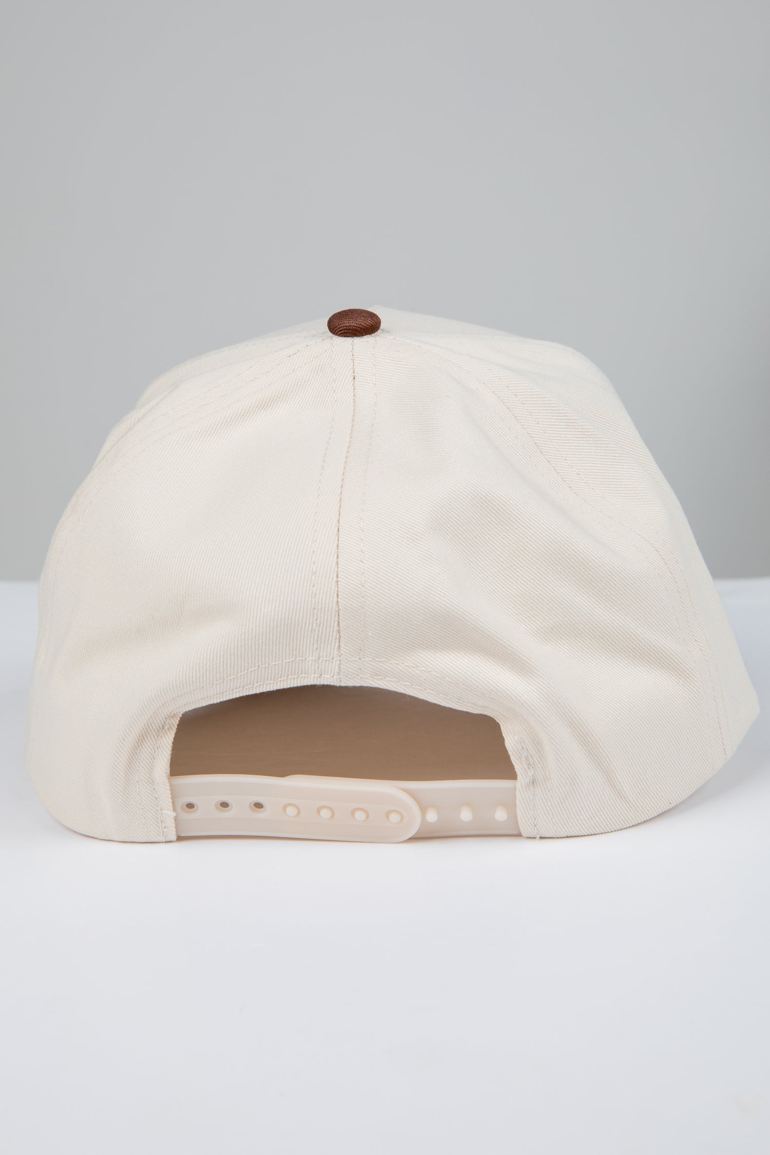 Beige baseball cap with a brown button on a light gray background