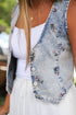 Denim vest with floral embroidery over a white top and pants, blurred background