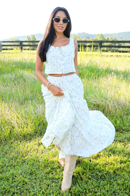 Woman in a white dress standing in a grassy field with mountains in the background