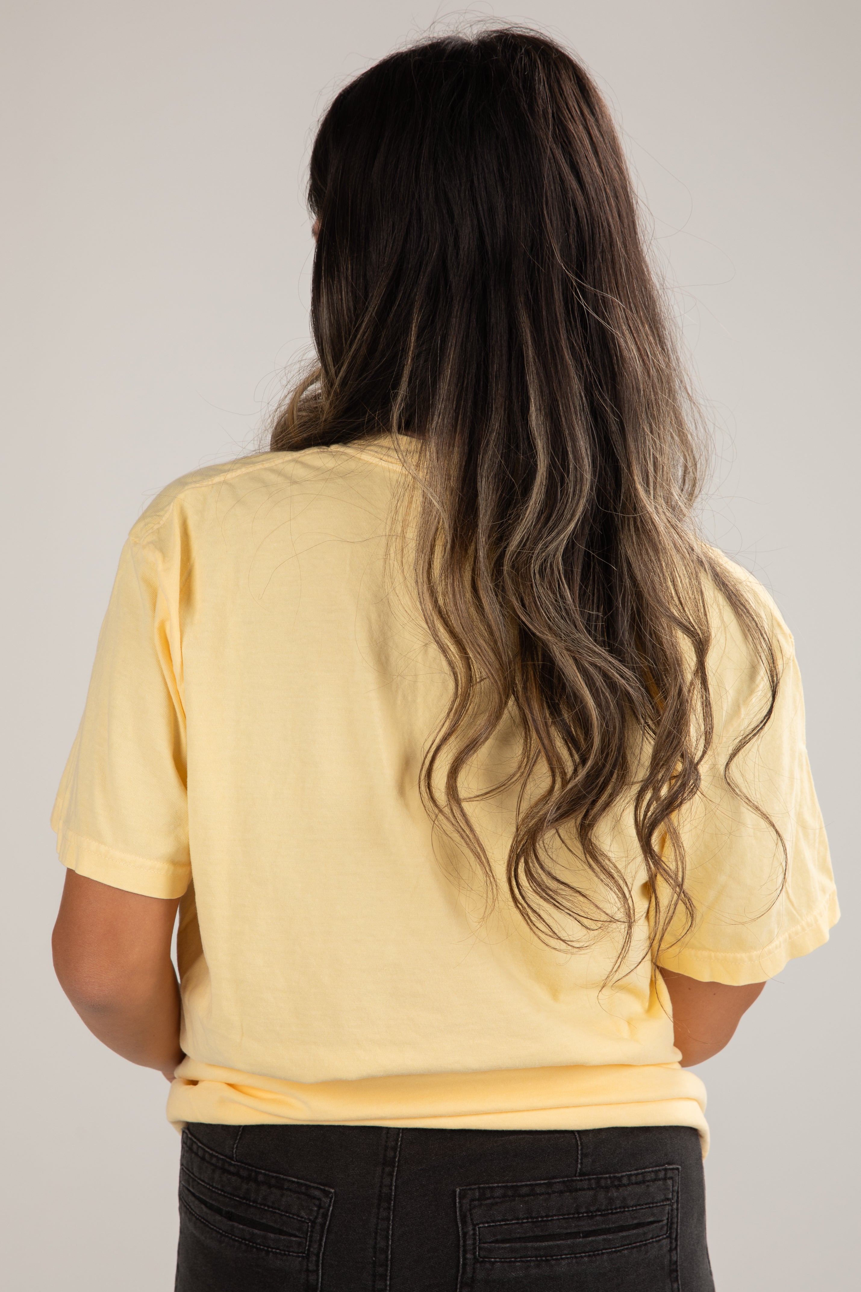 Person wearing a yellow t-shirt with long hair on a plain background