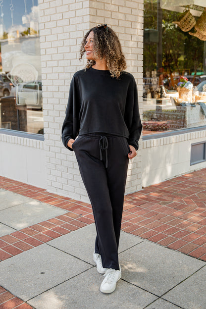 Woman in black outfit standing on a sidewalk with a building in the background