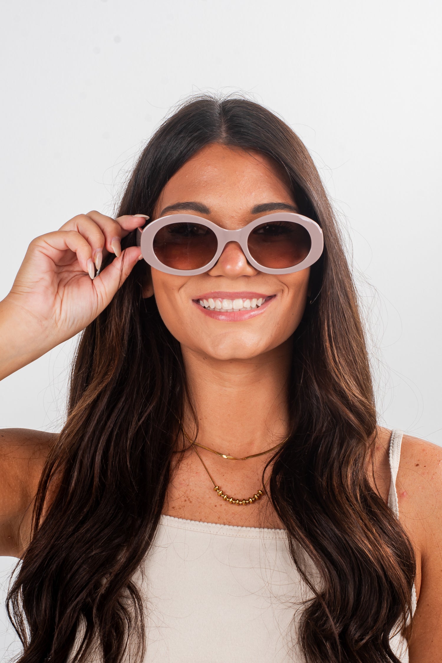 Woman holding a pair of sunglasses in front of her face against a white background